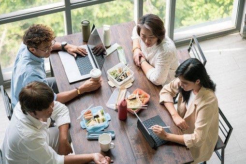 Group of coworkers having a working lunch with laptops and food.