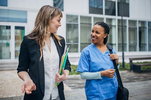 Business professional and healthcare worker talking outside a building.